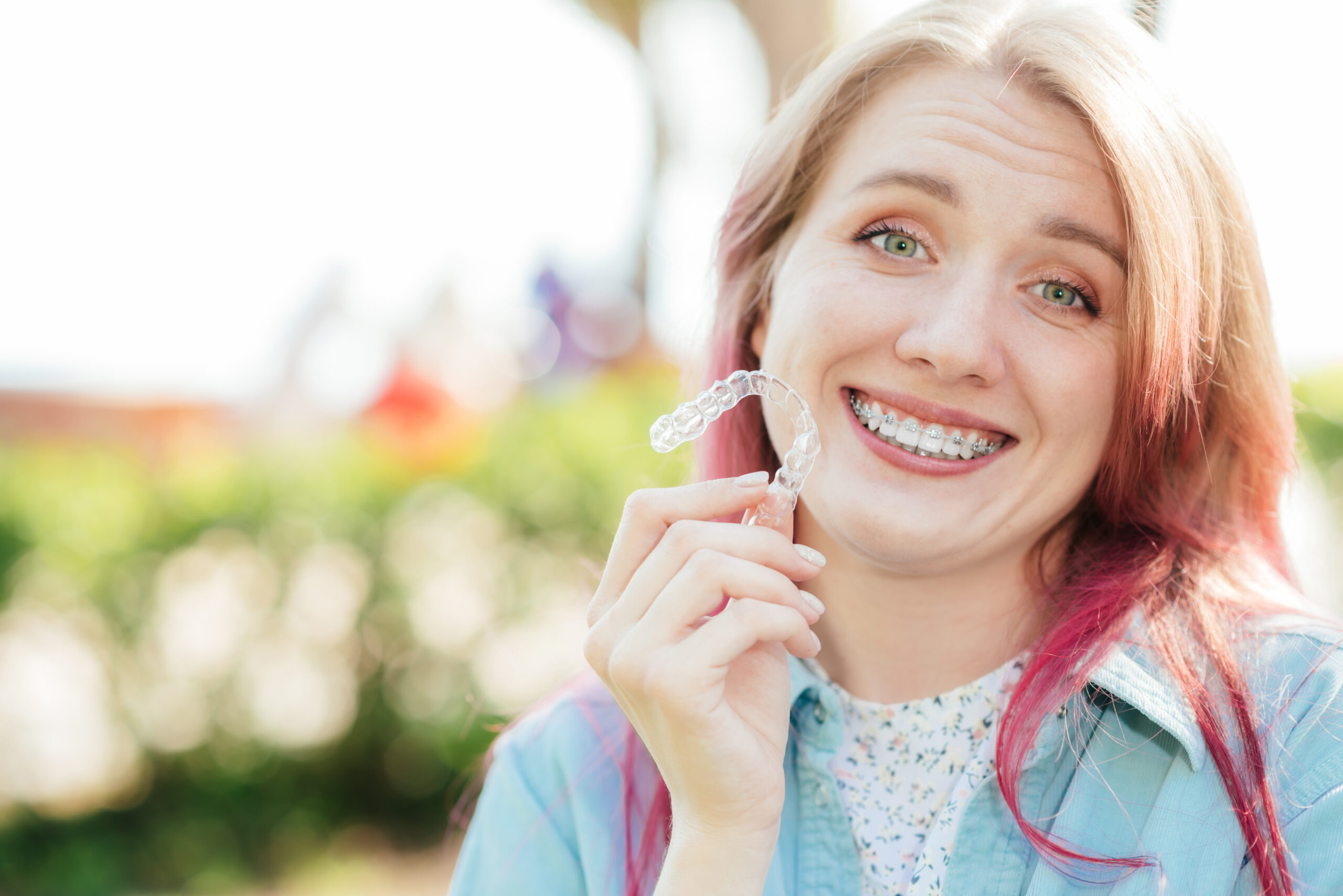 Dental care.Smiling girl with braces on her teeth holds aligners in her hands and shows the difference between them